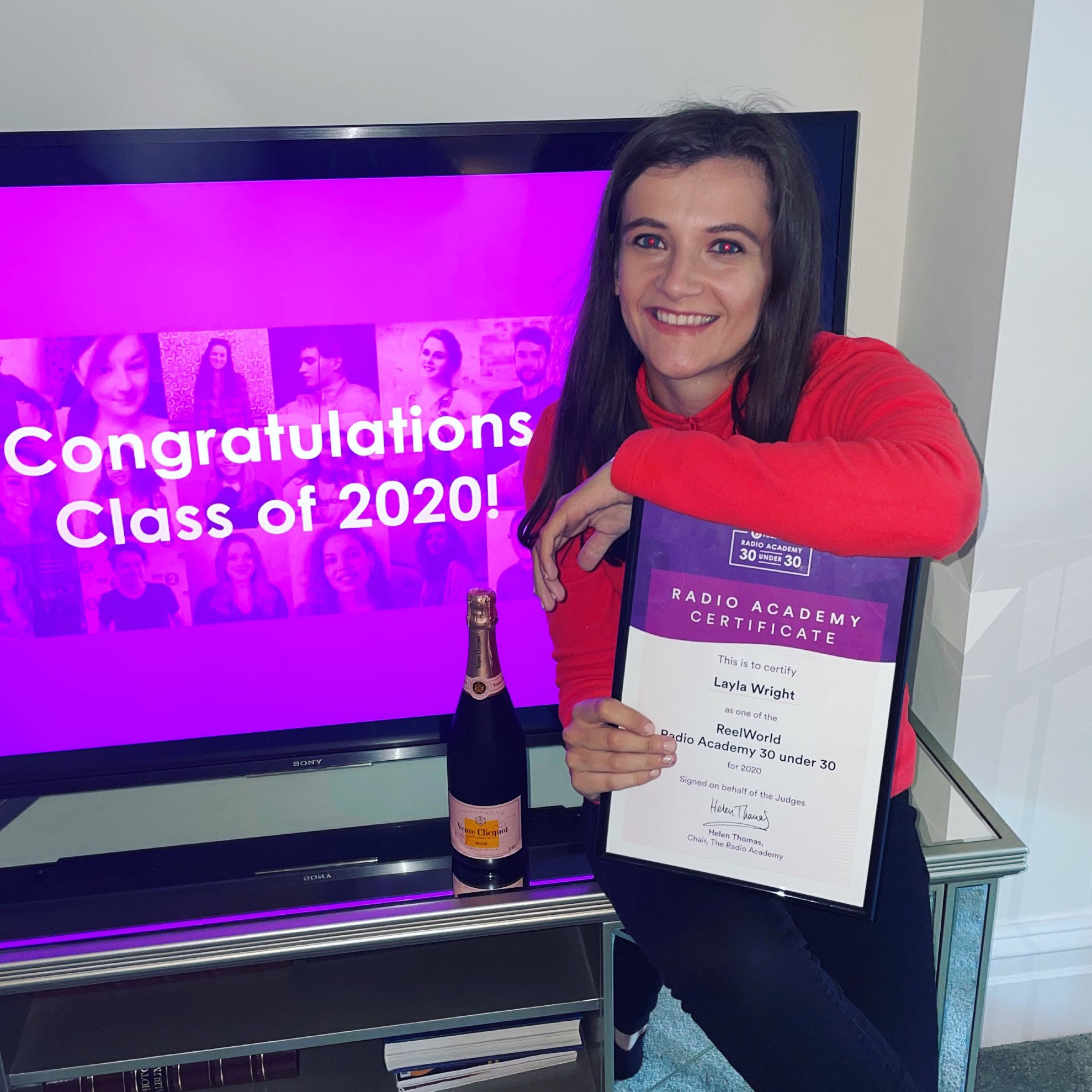 Layla smiling holding her framed certificate, in front of a screen that reads 'congratulations class of 2020'